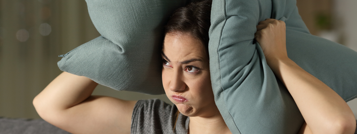 Femme se bouchant les oreilles avec des oreillers pour se protéger des troubles de voisinage en copropriété