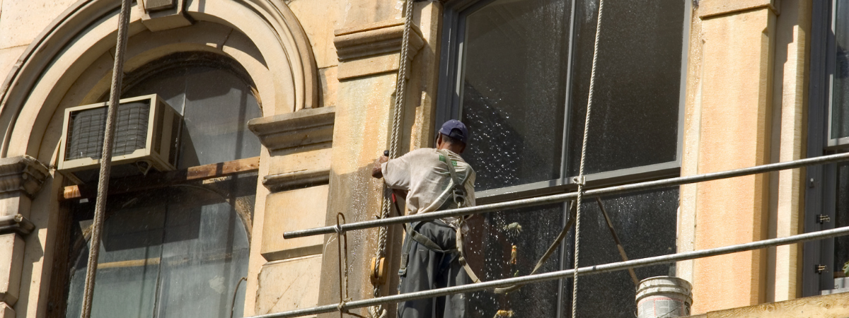 Une personne sur un échafaudage en train de nettoyer la façade d'un immeuble représentant l'entretien extérieur d'une copropriété