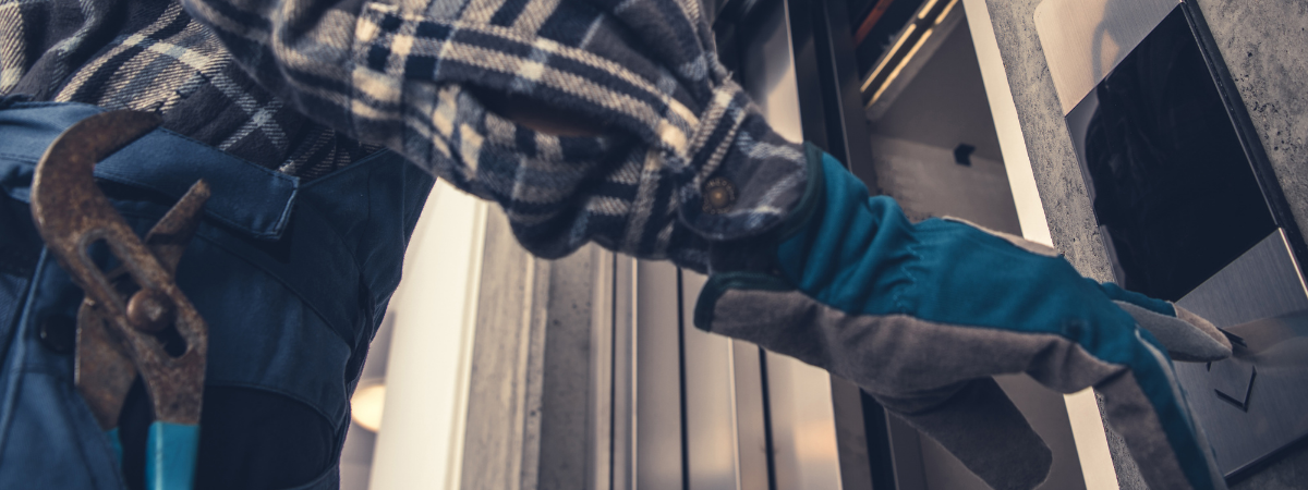 Ouvrier en train d'appuyer sur le bouton d'un ascenseur représentant la maintenance des équipements communs dans une copropriété